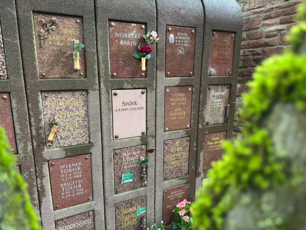 Nahaufnahme einer mit Kolumbariumwand auf dem Hauptfriedhof Frankfurt am Main mit eingravierten Gedenktafeln, die teilweise mit Blumen und kleinen Erinnerungsstücken verziert sind.